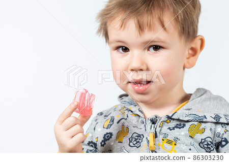 Cute little boy with blond hair is holding a pink dental myofunctional trainer Cute little boy with blond hair is holding a pink dental myofunctional trainer 86303230