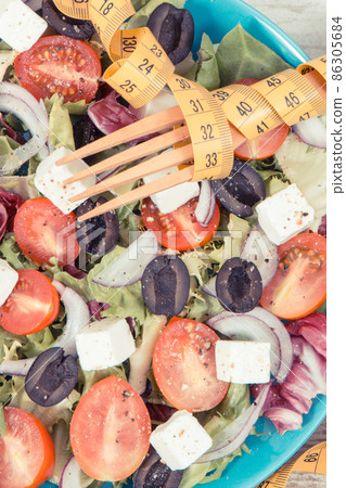 Tape measure and greek salad with feta cheese and vegetables as healthy meal containing vitamins Tape measure and greek salad with feta cheese and vegetables as healthy meal containing vitamins 86305684