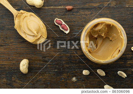 Wooden spoon with a jar of peanut butter and a bunch of scattered nuts Wooden spoon with a jar of peanut butter and a bunch of scattered nuts 86306096