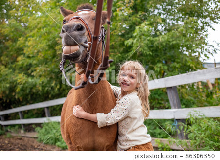 little girl hugs pony horse in corral and laugh happy 86306350
