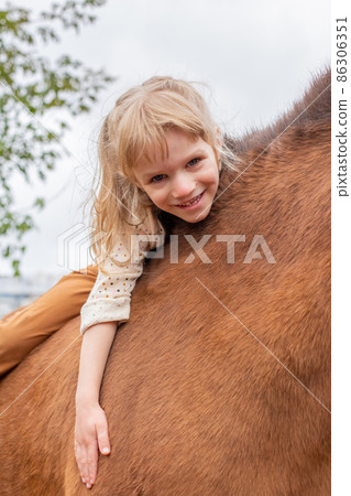 little girl hugs pony horse and laugh happily 86306351