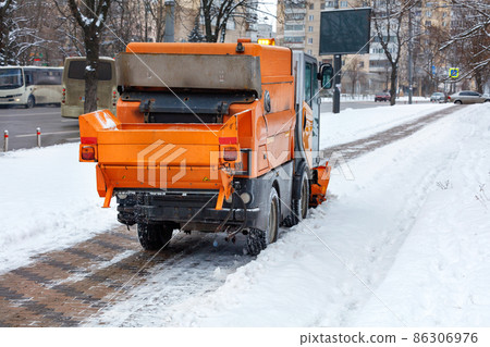 The sweeper cleans the snow on the cobbled sidewalk of the city street. 86306976