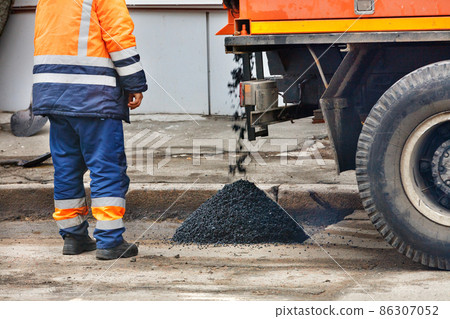 A road worker stands next to a truck pouring fresh asphalt onto a repaired section of road. A road worker stands next to a truck pouring fresh asphalt onto a repaired section of road. 86307052