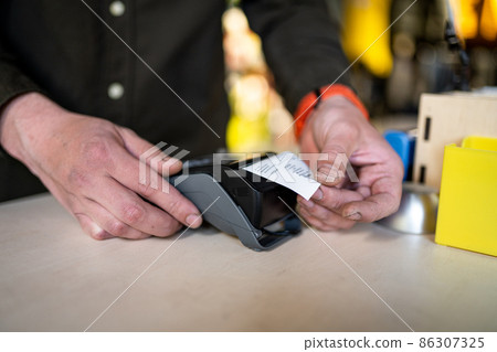 Salesman holds payment terminal while holding receipt for completing purchase. Hands close up. Concept of NFC, business and banking transactions. Payment terminal with paper tape. Bank terminal Salesman holds payment terminal while holding receipt for completing purchase. Hands close up. Concept of NFC, business and banking transactions. Payment terminal with paper tape. Bank terminal 86307325