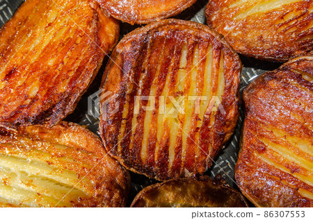 Baked hot potatoes with a golden crust on a baking sheet. 86307553