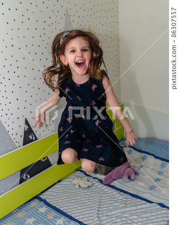 A little girl is jumping and playing in her room on the bed and laughing. A little girl is jumping and playing in her room on the bed and laughing. 86307557