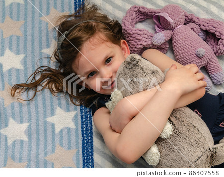 A little girl hugs her soft toys on the bed in her room. 86307558