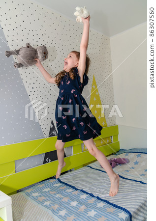 A little girl is jumping and playing in her room on the bed and laughing. A little girl is jumping and playing in her room on the bed and laughing. 86307560