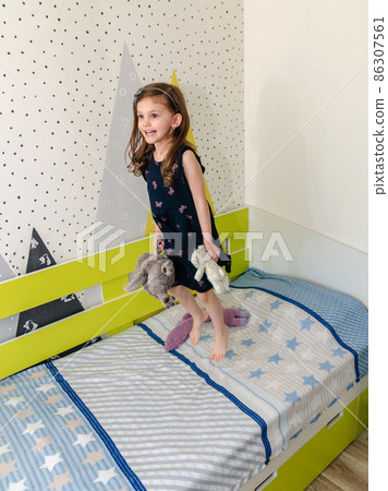 A little girl is jumping and playing in her room on the bed and laughing. A little girl is jumping and playing in her room on the bed and laughing. 86307561