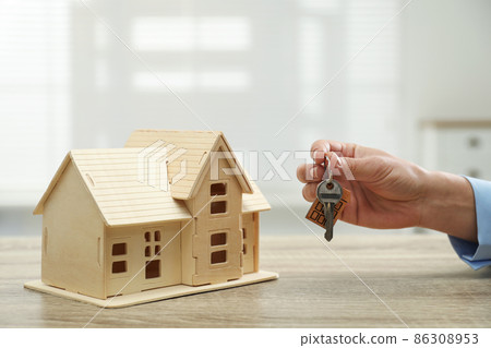 Real estate agent with house model and key at wooden table, closeup Real estate agent with house model and key at wooden table, closeup 86308953