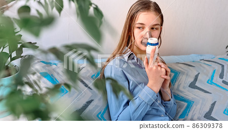 Teenage girl makes inhalation with a nebulizer equipment. Sick child holding inhalator in hand and breathes through an inhaler at home Teenage girl makes inhalation with a nebulizer equipment. Sick child holding inhalator in hand and breathes through an inhaler at home 86309378