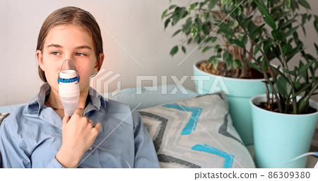 Teenage girl makes inhalation with a nebulizer equipment. Sick child holding inhalator in hand and breathes through an inhaler at home 86309380