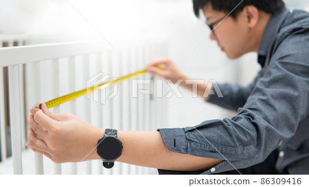 Asian man using tape measure on toddler bed rails Asian man using tape measure on toddler bed rails 86309416
