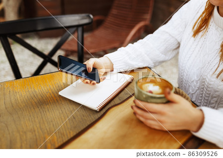 Woman holding a smartphone with empty screen sitting outdoors at the cafe with coffee on the table.Remote work concept. Woman holding a smartphone with empty screen sitting outdoors at the cafe with coffee on the table.Remote work concept. 86309526