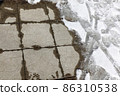 Melting snow on the paving slabs during spring thaw. Patch of sidewalk in thawing snow. 86310538