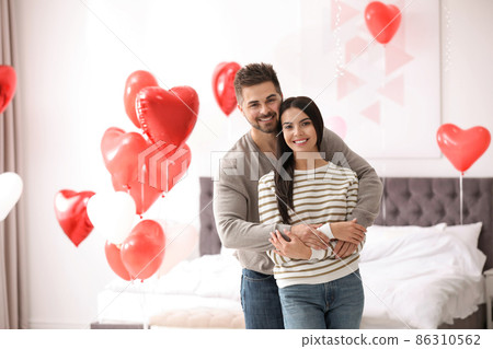 Lovely young couple in bedroom decorated with heart shaped balloons. Valentine's day celebration 86310562