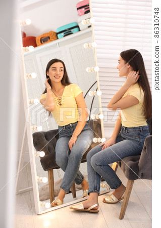 Beautiful young woman looking at herself in large mirror indoors 86310748