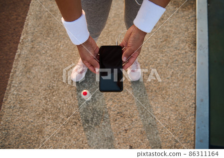 Top view of female athlete hands in white terry wristbands holding a smartphone with empty blank black screen and browsing on websites and mobile applications. 86311164