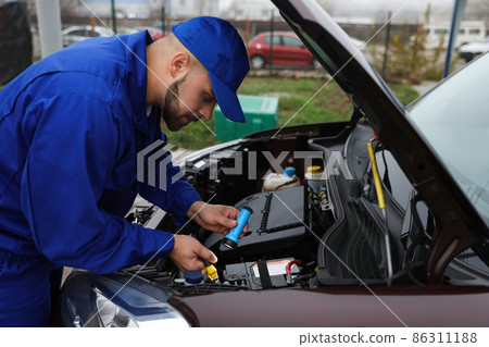 Young mechanic with flashlight fixing car outdoors 86311188