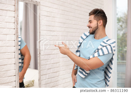 Young man looking at himself in large mirror at home 86311190