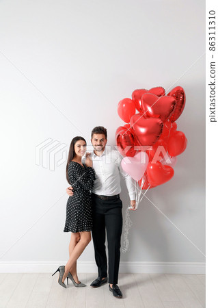 Young man presenting gift to his girlfriend in bedroom decorated with heart shaped balloons 86311310