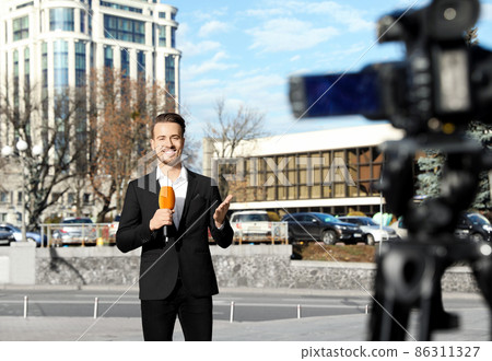 Young male journalist with microphone working on city street 86311327