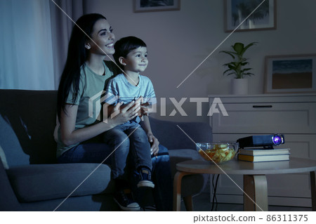 Young mother and her son watching movie using video projector at home Young mother and her son watching movie using video projector at home 86311375