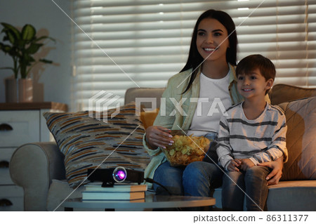 Young woman and her son watching movie using video projector at home. Space for text 86311377