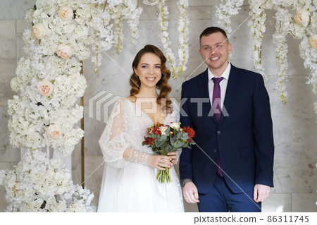 beautiful and happy bride and groom in an arch of flowers at wedding ceremony beautiful and happy bride and groom in an arch of flowers at wedding ceremony 86311745