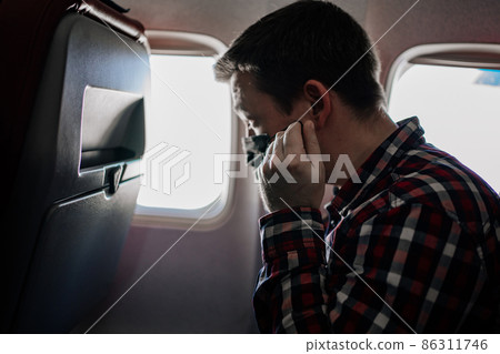 man corrects a black protective mask and plaid shirt by the window on the plane. man corrects a black protective mask and plaid shirt by the window on the plane. 86311746