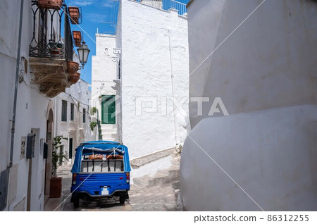 Ostuni, Puglia, Italy. August 2021. Amazing view on one of the white alleys of the old town. A blue-colored tourist truck is in the middle of the alley. Ostuni, Puglia, Italy. August 2021. Amazing view on one of the white alleys of the old town. A blue-colored tourist truck is in the middle of the alley. 86312255