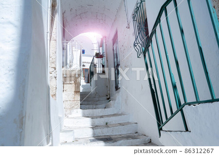 Ostuni, Puglia, Italy. August 2021. Amazing view on one of the white alleys of the old town. The unique charm of the place, white as the dominant color, the sense of peace and tranquility. 86312267