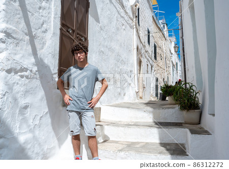 Ostuni, Puglia, Italy. August 2021. A young Caucasian is posing for a souvenir photo in one of the white alleys of the historic center of the village. Concept of young people on vacation. 86312272