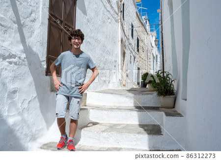 Ostuni, Puglia, Italy. August 2021. A young Caucasian is posing for a souvenir photo in one of the white alleys of the historic center of the village. Concept of young people on vacation. 86312273