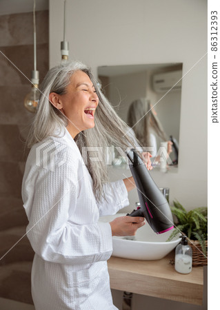 Happy woman styling hair after taking a bath 86312393