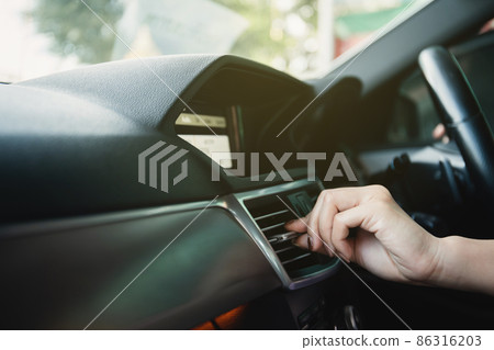 Woman adjusting an air grille on the vehicle dashboard while driving on the road during the rain. Climate control system in the modern car with cool and warm air conditioner. Temperature control. 86316203