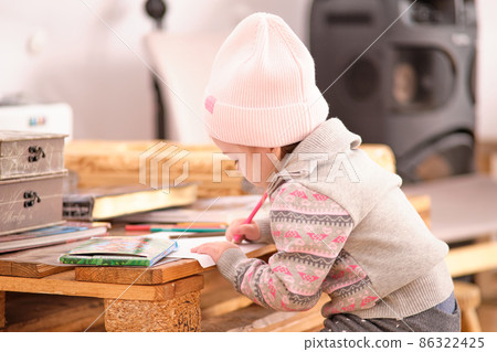 A little girl draws with felt-tip pens on a table made of wooden pallets. A little girl draws with felt-tip pens on a table made of wooden pallets. 86322425