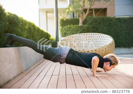 Active Asian young man making an outdoor body weight exercise close up, sportsman doing body weight workout by pushup and plank. Asian sportsman exercising for muscle and body building. 86323776