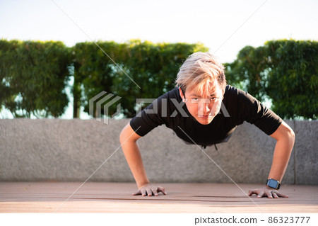 Active Asian young man making an outdoor body weight exercise close up, sportsman doing body weight workout by pushup and plank. Asian sportsman exercising for muscle and body building. 86323777