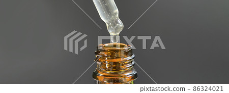 Pipette with a drop of face serum or oil for the face and hyaluronic acid on beautiful black background, close-up. 86324021
