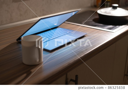 A working laptop with a white screen stands on the kitchen table next to the stove in the dark. The concept of remote work. Quarantine during coronavirus. 86325838