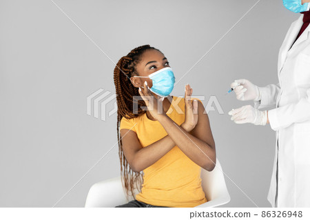 Young black woman in medical face mask stopping doctor from making covid vaccine shot on grey studio background 86326948