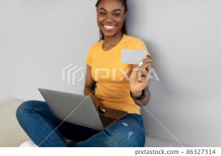 Happy African American woman with laptop showing empty credit card at camera against grey studio wall, mockup Happy African American woman with laptop showing empty credit card at camera against grey studio wall, mockup 86327314