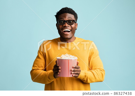 Excited black guy holding basket with popcorn, using 3d glasses Excited black guy holding basket with popcorn, using 3d glasses 86327438