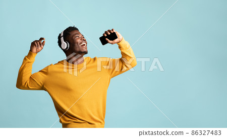 Joyful black guy singing songs, using headphones and smartphone Joyful black guy singing songs, using headphones and smartphone 86327483