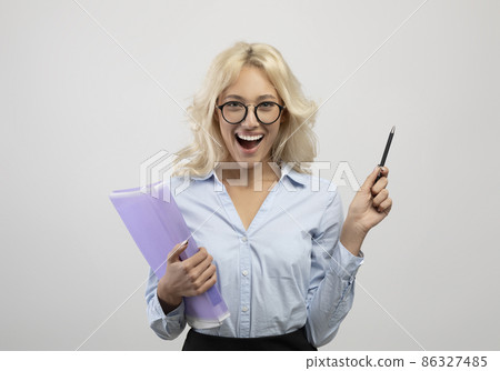 Overjoyed female entrepreneur in formal wear holding folder with documents and pen, posing over ligth grey background Overjoyed female entrepreneur in formal wear holding folder with documents and pen, posing over ligth grey background 86327485
