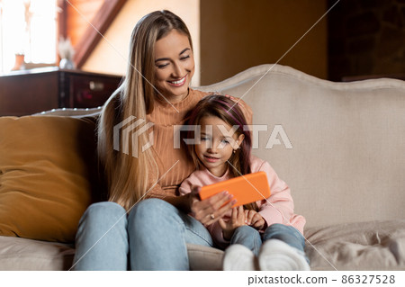 Smiling woman and girl using cellphone at home Smiling woman and girl using cellphone at home 86327528