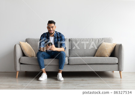 Portrait of smiling Arab man using smartphone at home Portrait of smiling Arab man using smartphone at home 86327534