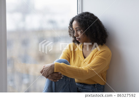 Unhappy young black woman looking out window, having depressive thoughts at home, copy space Unhappy young black woman looking out window, having depressive thoughts at home, copy space 86327592
