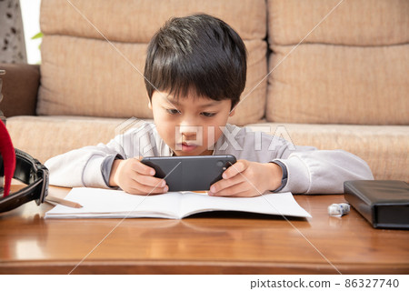 Elementary school boy looking at a smartphone while studying Elementary school boy looking at a smartphone while studying 86327740